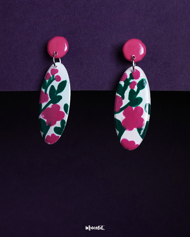 Nargis floral drop earrings displayed against a dual-tone purple background, highlighting the hand-painted pink and green floral patterns on white ovals, showcasing the charm of handmade artistry — Muselot.