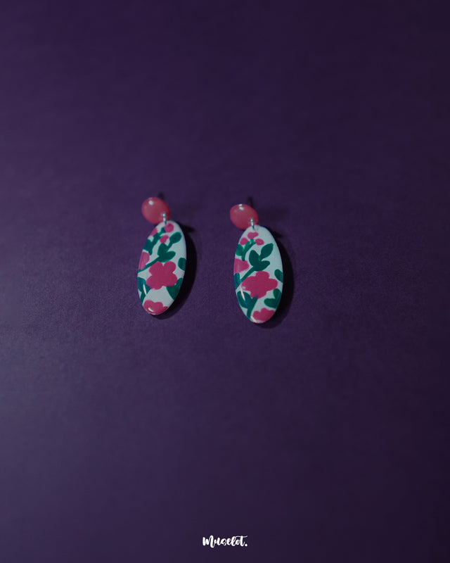Nargis pink floral drop earrings displayed against a purple background, highlighting the hand-painted rose pink floral motifs and glossy finish that showcase their playful charm and artisanal elegance — Muselot.