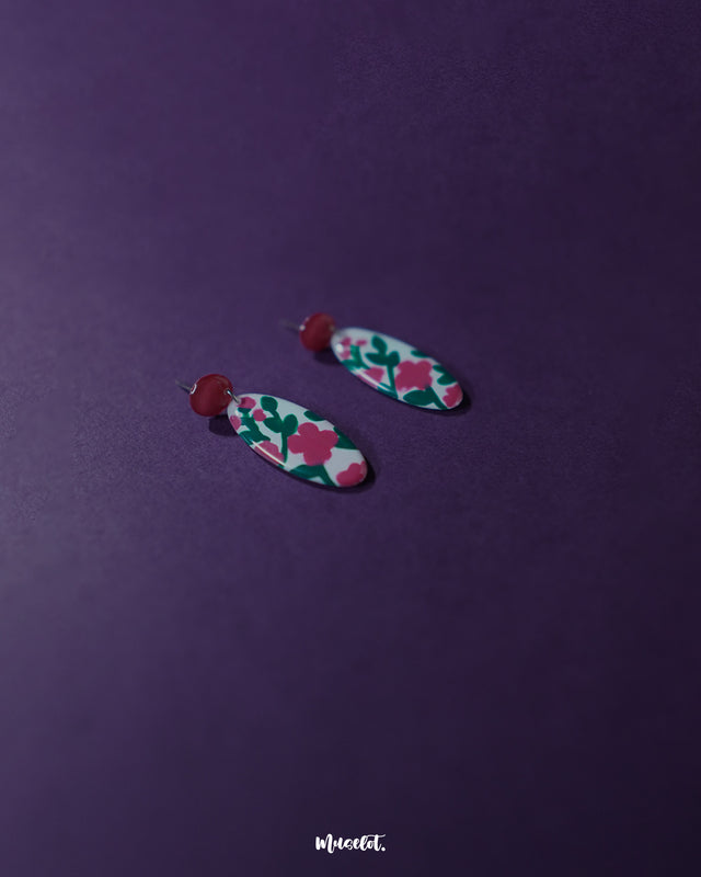 Side view of the Nargis pink floral drop earrings placed against a soft background, showcasing the curved floral design and elegant color contrast that adds charm to handmade jewelry — Muselot.