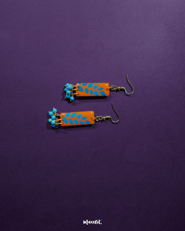 A Narmshaam handmade hook earrings placed against a soft fabric background, highlighting the intricate handwoven pattern and the earthy tones that lend a calm, artistic charm to everyday styling — Muselot.