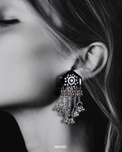 Close-up of model wearing Nazafar black handcrafted earrings, showcasing white circular detailing and cascading silver ghungroo chains – Muselot.