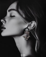 Model wearing Nazafar black handcrafted earrings, featuring white painted motifs and layered silver ghungroo chains for a striking traditional look – Muselot.