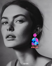 A woman wearing the Neelzair handmade purple floral earrings turns slightly to the side, highlighting the playful pink bead dangles and showcasing the vibrant hand-painted florals that elevate the accessory’s charm — Muselot.