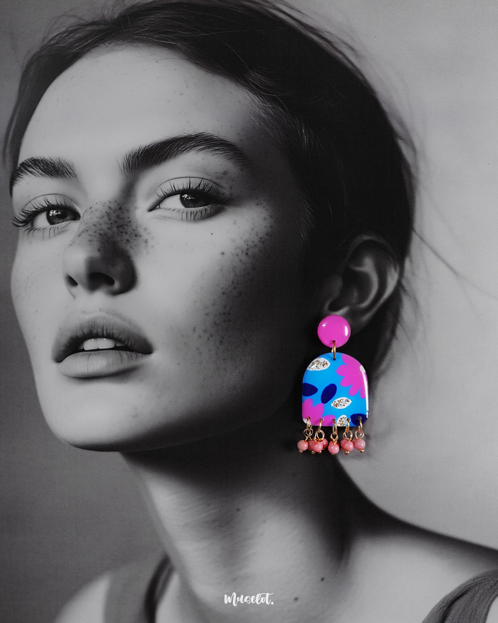 A woman wearing the Neelzair handmade purple floral earrings turns slightly to the side, highlighting the playful pink bead dangles and showcasing the vibrant hand-painted florals that elevate the accessory’s charm — Muselot.