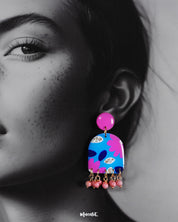 Closeup of a woman wearing the Neelzair handmade purple floral earrings, highlighting the glossy finish, bold pink and blue floral patterns, and delicate hanging beads that showcase their intricate handcrafted charm — Muselot.
