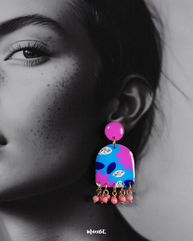 Closeup of a woman wearing the Neelzair handmade purple floral earrings, highlighting the glossy finish, bold pink and blue floral patterns, and delicate hanging beads that showcase their intricate handcrafted charm — Muselot.