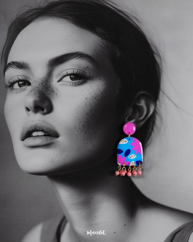 A woman wearing the Neelzair handmade purple floral earrings turns slightly to the side, highlighting the playful pink bead dangles and showcasing the vibrant hand-painted florals that elevate the accessory’s charm — Muselot.