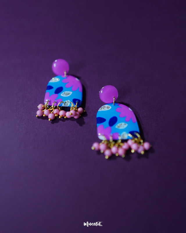 Close-up of Neelzair purple floral earrings featuring hand-painted pink and blue florals with delicate golden specks, highlighting the artisanal detailing and showcasing the charm of the pink beaded danglers — Muselot.