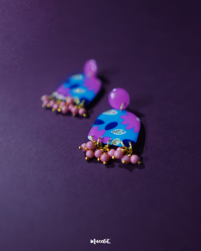 The Neelzair purple floral earrings are displayed against a soft backdrop, highlighting their layered flower design and dangling bead accents that showcase vibrant handmade artistry — Muselot.