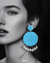 Close-up of model wearing the Neerangi pearl earrings, showcasing small and large round turquoise blue discs with delicate silver glitter accents, finished with dangling white pearl-like beads, highlighting their elegant and vibrant design – Muselot.