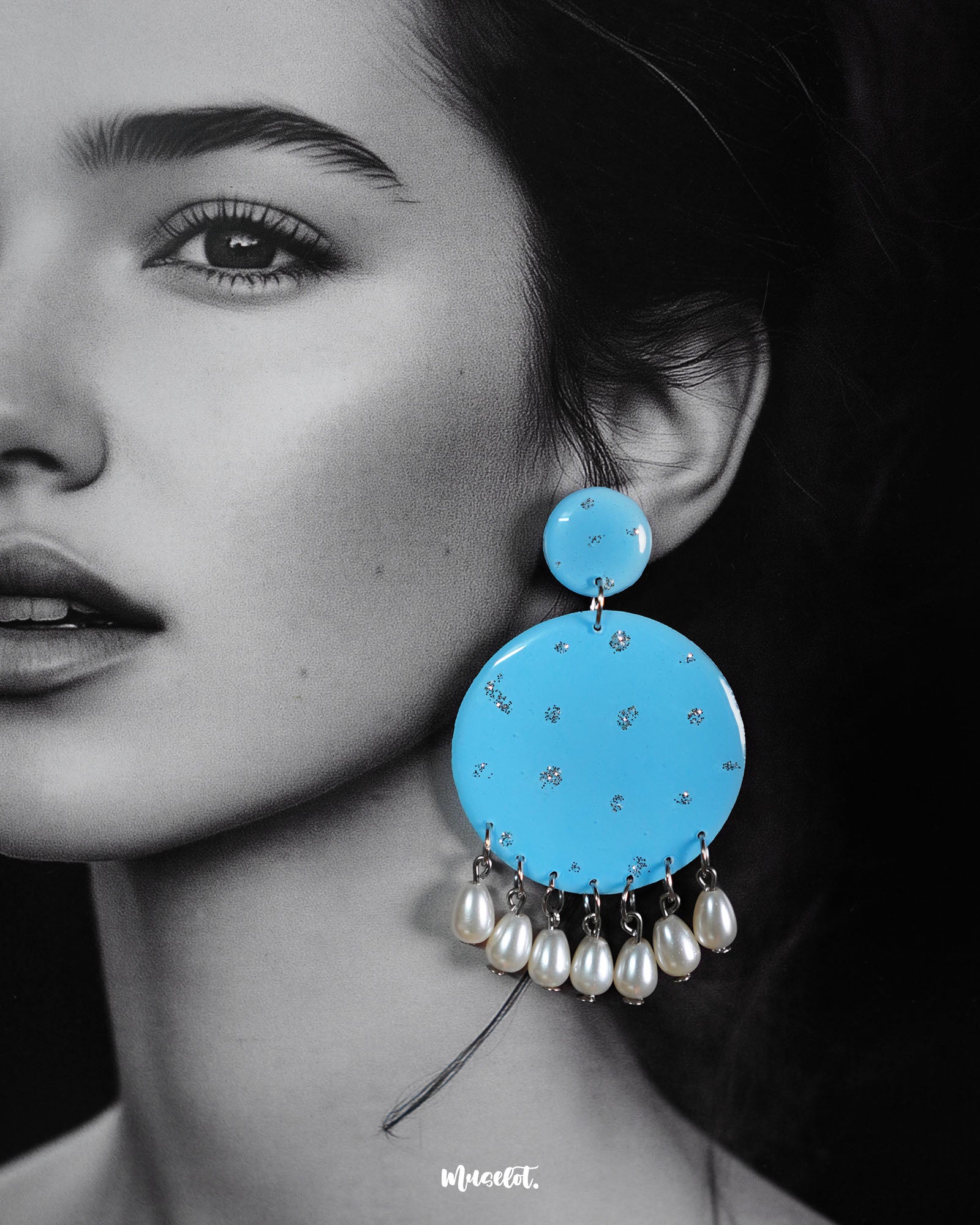 Close-up of model wearing the Neerangi pearl earrings, showcasing small and large round turquoise blue discs with delicate silver glitter accents, finished with dangling white pearl-like beads, highlighting their elegant and vibrant design – Muselot.