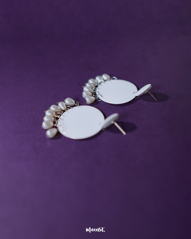 Noor white drop earrings displayed against a muted backdrop, showcasing their graceful arc and suspended pearl accents that highlight refined sophistication — Muselot.