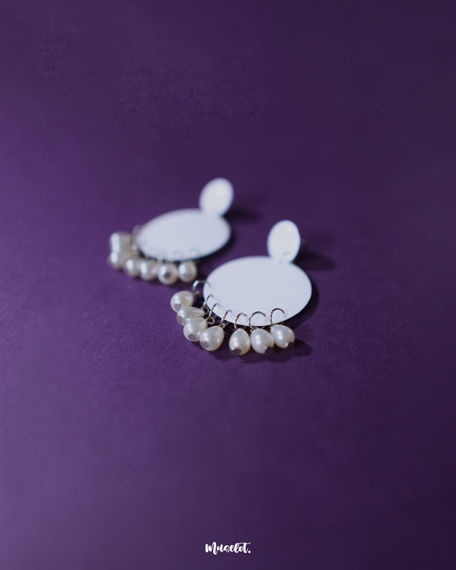 Close-up of Noor white drop earrings featuring delicate pearl-like beads and a crescent-shaped frame, highlighting intricate detailing and showcasing graceful, handcrafted elegance — Muselot.