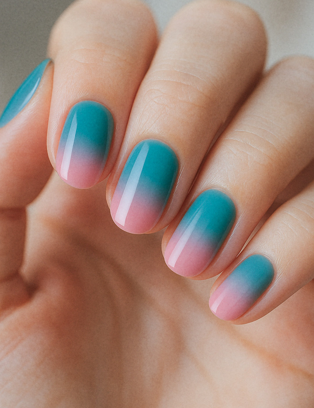 A shot of a model’s hand wearing Ocean Sunset ombre nail stickies, blending a refreshing teal blue into soft pink with a smooth glossy gradient, capturing the calm yet vibrant charm of sunset-inspired ombre nail art – Muselot.