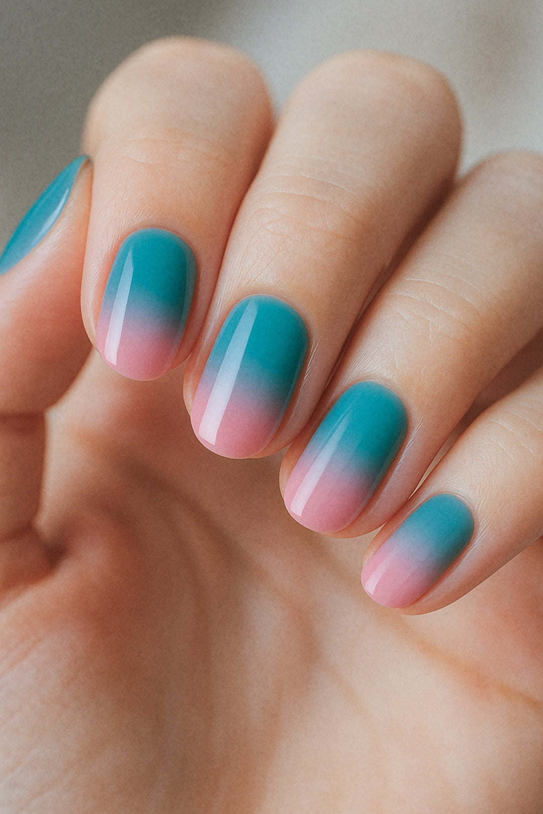 A shot of a model’s hand wearing Ocean Sunset ombre nail stickies, blending a refreshing teal blue into soft pink with a smooth glossy gradient, capturing the calm yet vibrant charm of sunset-inspired ombre nail art – Muselot.
