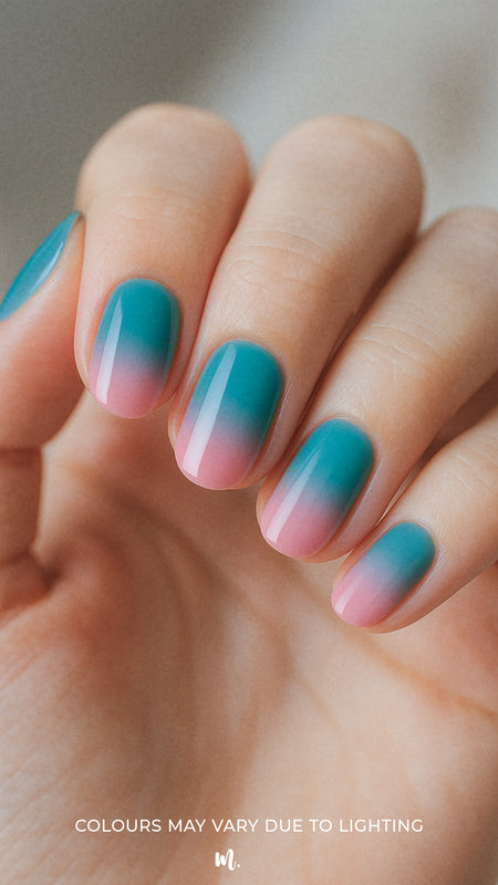 A shot of a model’s hand wearing Ocean Sunset ombre nail stickies, blending a refreshing teal blue into soft pink with a smooth glossy gradient, capturing the calm yet vibrant charm of sunset-inspired ombre nail art – Muselot.