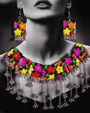 A close-up of the model wearing the Parizad floral jewelry set, showing the colorful hand-painted flowers on a black base. The silver gungroo details add a soft, playful charm, while the vibrant design brightens up the neckline — Muselot.