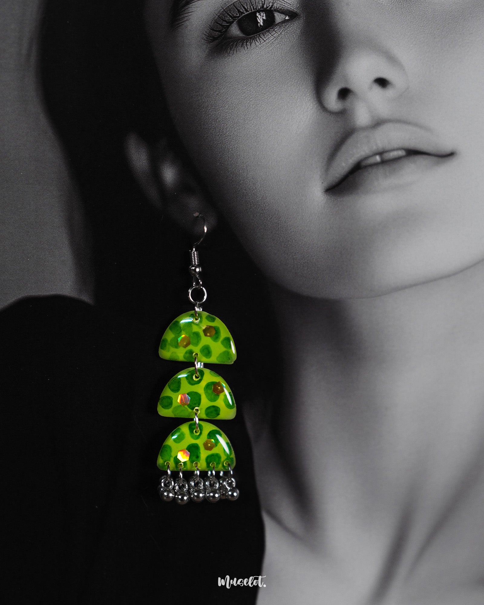 Close-up of a woman wearing the Parvaaz handmade green drop earrings, emphasizing their glossy triple-tiered semicircle form and delicate hand-painted botanical dots, highlighting whimsical charm and showcasing artistic craftsmanship — Muselot.