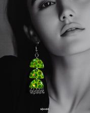 Close-up of a woman wearing the Parvaaz handmade green drop earrings, emphasizing their glossy triple-tiered semicircle form and delicate hand-painted botanical dots, highlighting whimsical charm and showcasing artistic craftsmanship — Muselot.