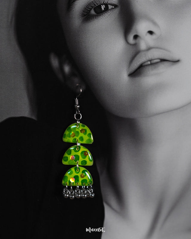 Close-up of a woman wearing the Parvaaz handmade green drop earrings, emphasizing their glossy triple-tiered semicircle form and delicate hand-painted botanical dots, highlighting whimsical charm and showcasing artistic craftsmanship — Muselot.