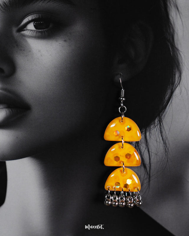 A close-up of a woman wearing Parvaaz handmade yellow drop earrings, highlighting their vibrant yellow tones and smooth, glossy finish. The delicate metallic chains add movement and charm, showcasing a bold and cheerful accessory perfect for statement styling — Muselot.