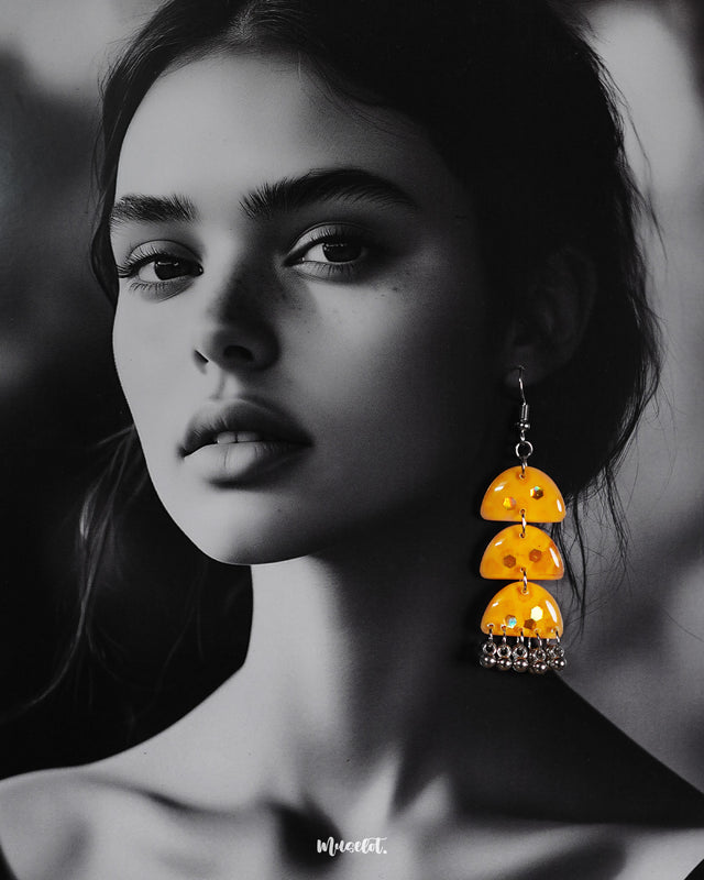 A woman wearing Parvaaz yellow drop earrings, the triple-tiered design featuring glossy yellow domes and metallic danglers, highlighting artisanal flair and showcasing bold statement style — Muselot.