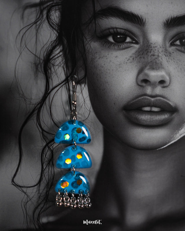 A close-up view of Parvaaz blue handmade drop earrings laid against a soft neutral backdrop, highlighting the vivid floral detailing and intricate brushwork that showcase the earrings' artisanal charm and colorful elegance — Muselot.