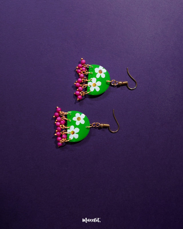 Phoolbaan floral hook earrings with white hand-painted flowers on a vibrant green base, finished with dangling magenta beads—highlighting playful elegance and showcasing handcrafted beauty — Muselot.