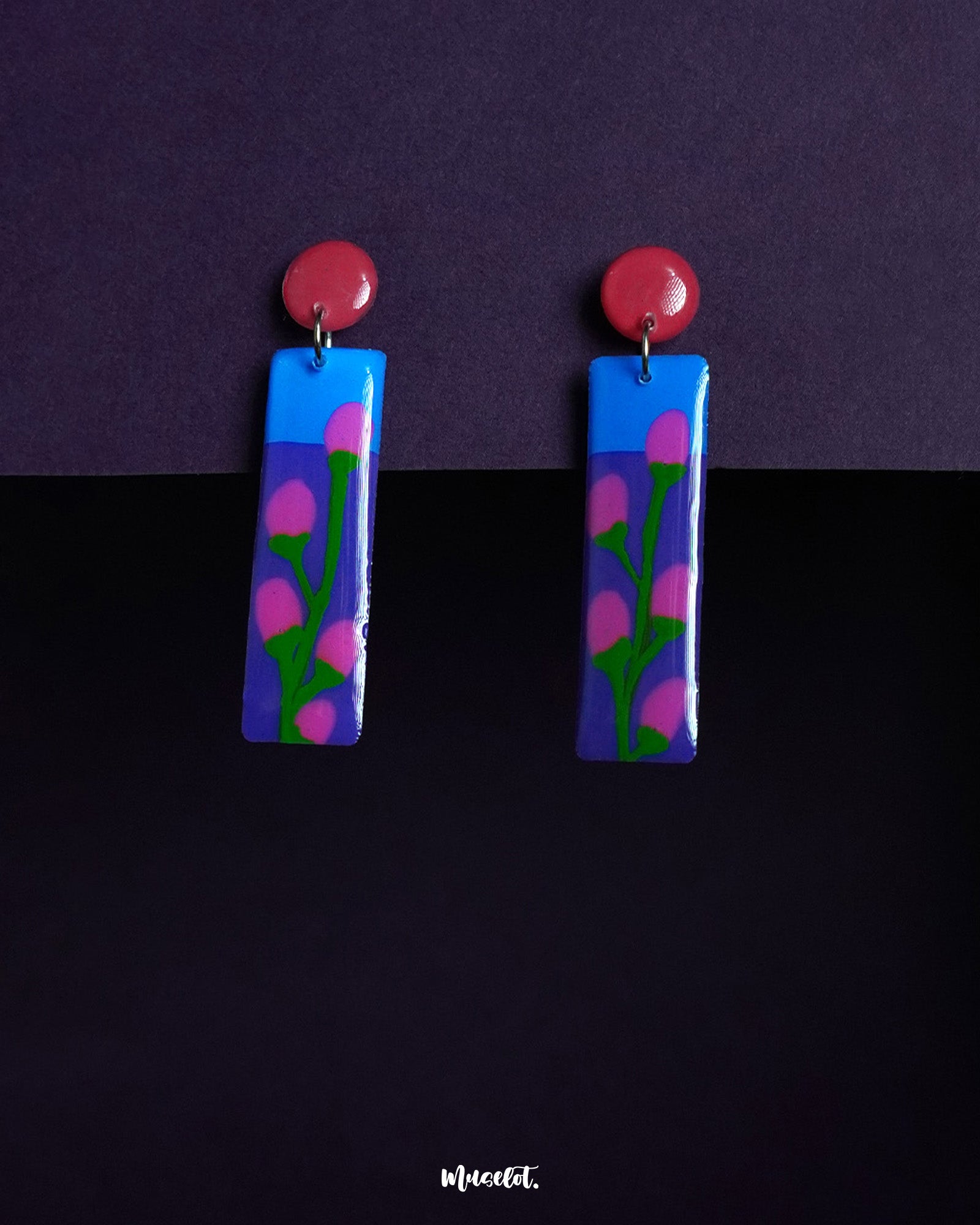 Raatgul drop earrings featuring a hand-painted floral design with bright pink buds and green stems against a vivid blue and purple base. The glossy finish and red circular tops create a playful, contemporary look perfect for bold expressions — Muselot.