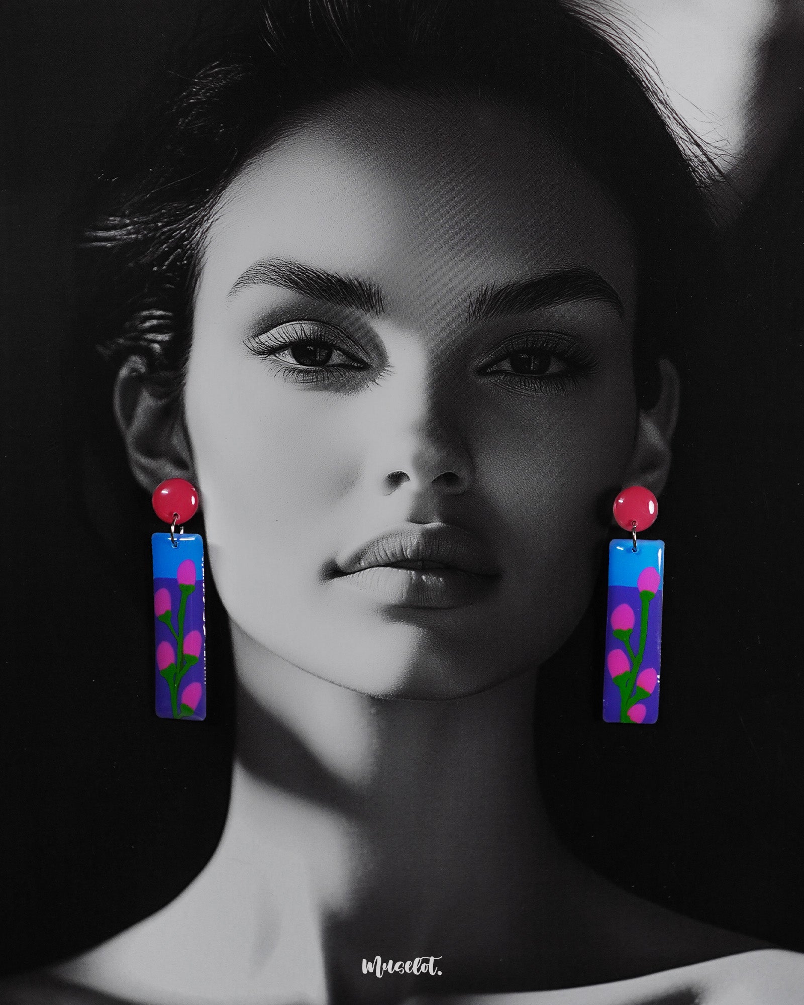 A woman wearing the Raatgul drop earrings brings them to life with effortless charm. The earrings’ glossy blue and purple panels, adorned with hand-painted pink buds and green stems, contrast beautifully with the bold red tops, adding a pop of artistic flair to her look — Muselot.