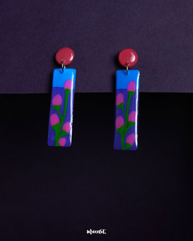 Raatgul drop earrings featuring a hand-painted floral design with bright pink buds and green stems against a vivid blue and purple base. The glossy finish and red circular tops create a playful, contemporary look perfect for bold expressions — Muselot.