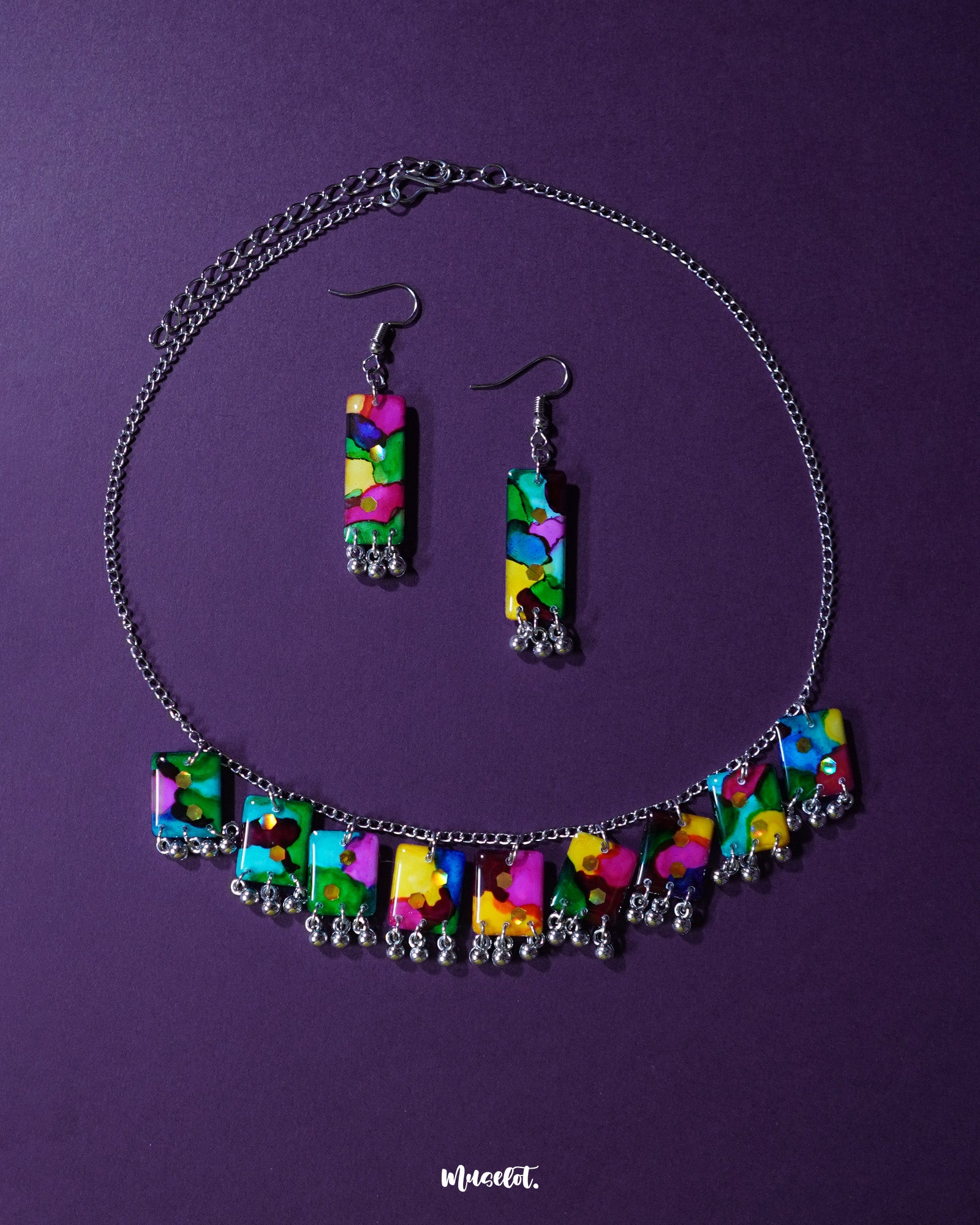 A vibrant handmade necklace set featuring colorful beads, playful ghungroos, and detailed threadwork is artfully arranged on a flat surface. The bold and festive tones of the jewelry evoke traditional Indian charm, making it a statement piece perfect for ethnic or boho-inspired looks – Muselot.