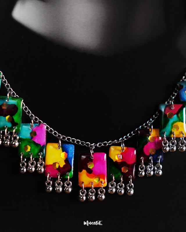 Model wearing the Rangbaari colorful jewelry set, featuring a silver chain necklace and matching earrings with vibrant multicolor abstract rectangular charms and silver bead accents, stylishly showcased to highlight its bold and artistic appeal – Muselot.