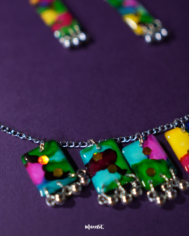 Rangbaari colorful jewelry set with a silver chain necklace and matching earrings, each adorned with vibrant multicolor rectangular charms and silver bead detailing, beautifully showcased on a rich purple backdrop – Muselot.