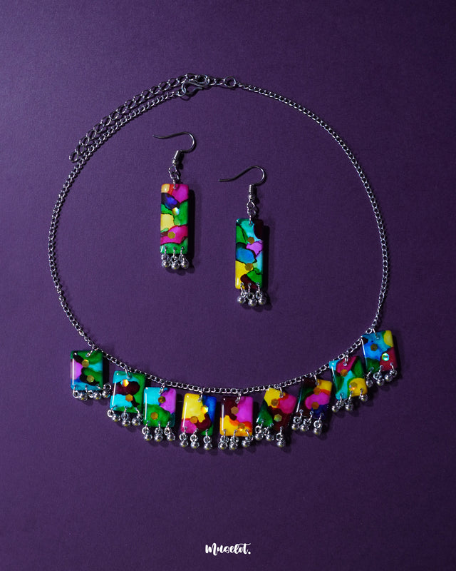 A vibrant handmade necklace set featuring colorful beads, playful ghungroos, and detailed threadwork is artfully arranged on a flat surface. The bold and festive tones of the jewelry evoke traditional Indian charm, making it a statement piece perfect for ethnic or boho-inspired looks – Muselot.