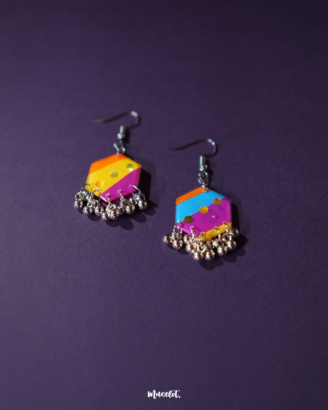 A pair of Rangbahaar colorful hook earrings displayed against a purple background, featuring a striking mix of orange, yellow, pink, and blue hues with hexagonal sequin details and silver-toned dangling beads for a playful, handcrafted charm — Muselot.