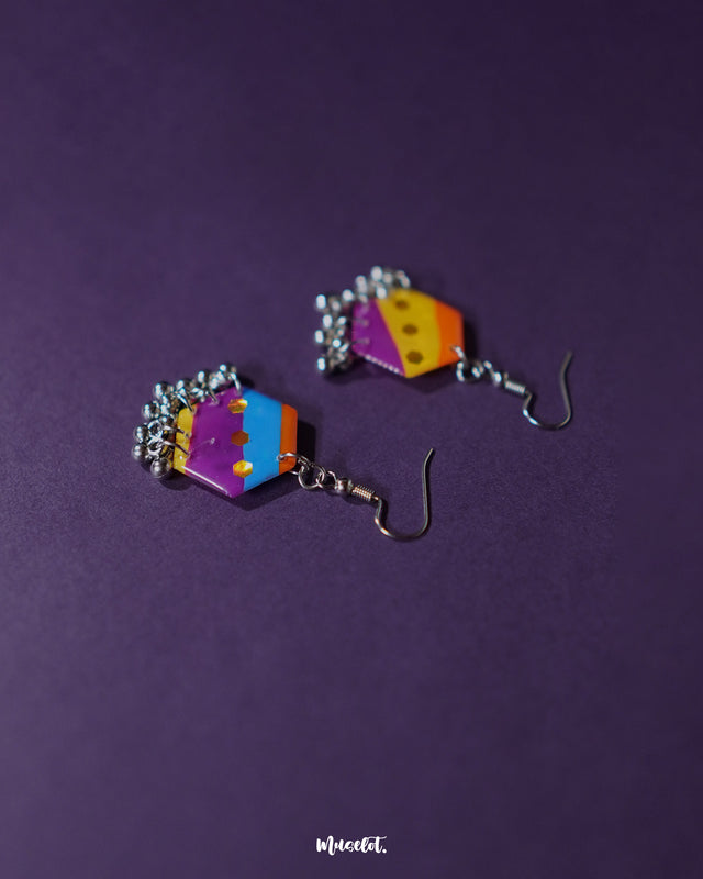 A pair of Rangbahaar colorful hook earrings rests gracefully, showcasing their geometric charm with bright multicolored threads, mirrored sequins, and delicate silver bead accents that add festive flair — Muselot.