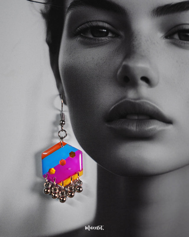 Close-up of a model wearing the Rangbahaar hook earrings, highlighting the vibrant geometric pattern in orange, yellow, pink, and blue, accented with reflective sequins and silver-toned dangling beads that enhance the festive flair — Muselot.