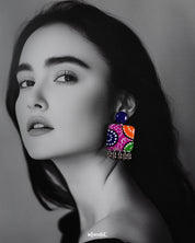 a model wearing Rangras folk art stud earrings, highlighting the vibrant colors and detailed patterns that bring a fusion of cultural heritage and contemporary elegance to the overall style — Muselot.