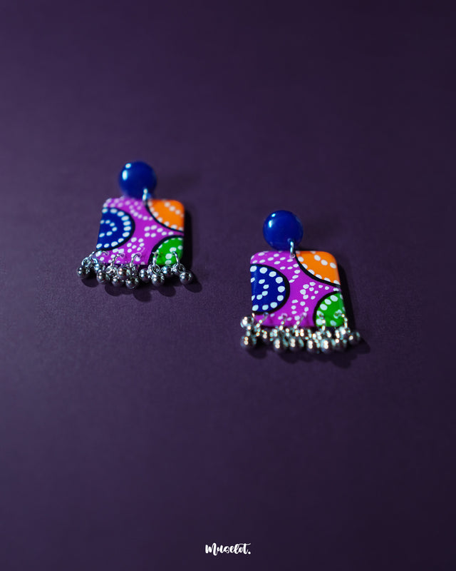 Rangras stud earrings displayed on a soft lavender-toned backdrop, highlighting their colorful hand-painted folk motifs and bold circular silhouette — a statement of vibrant artistry and culture — Muselot
