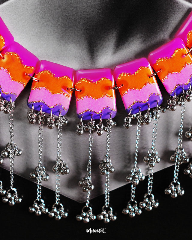A woman wears the Rangrezan handmade colorful necklace, its vivid chevron beads in pink, orange, purple, and blue gracefully lining her neckline, while silver-toned accents add a traditional charm to the bold, bohemian vibe — Muselot.