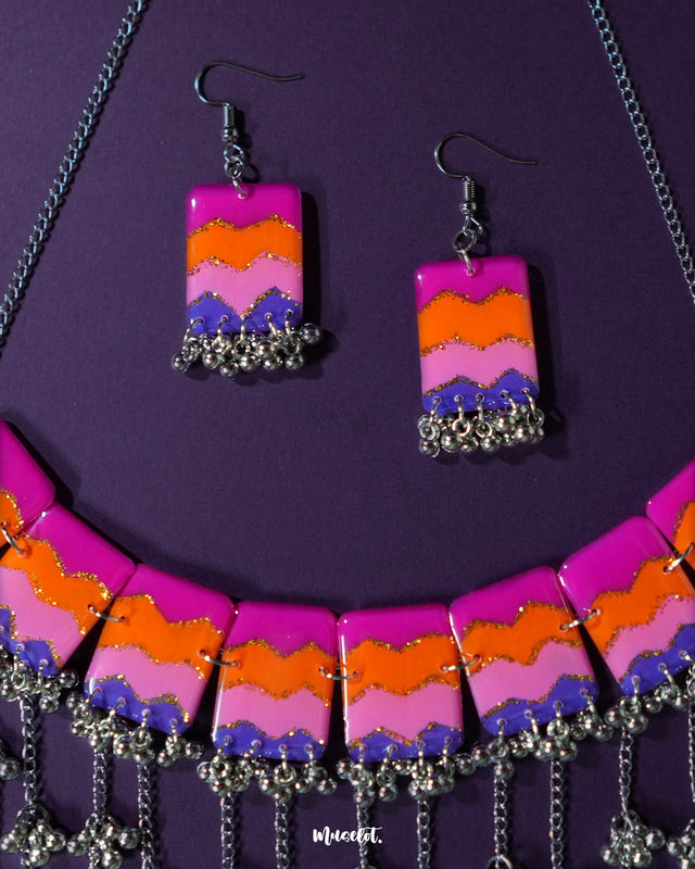 A pair of handcrafted earrings from the Rangrezan set rest against a purple background, showcasing their vivid beadwork and lively colors that mirror the joyful spirit of traditional Indian aesthetics — Muselot.