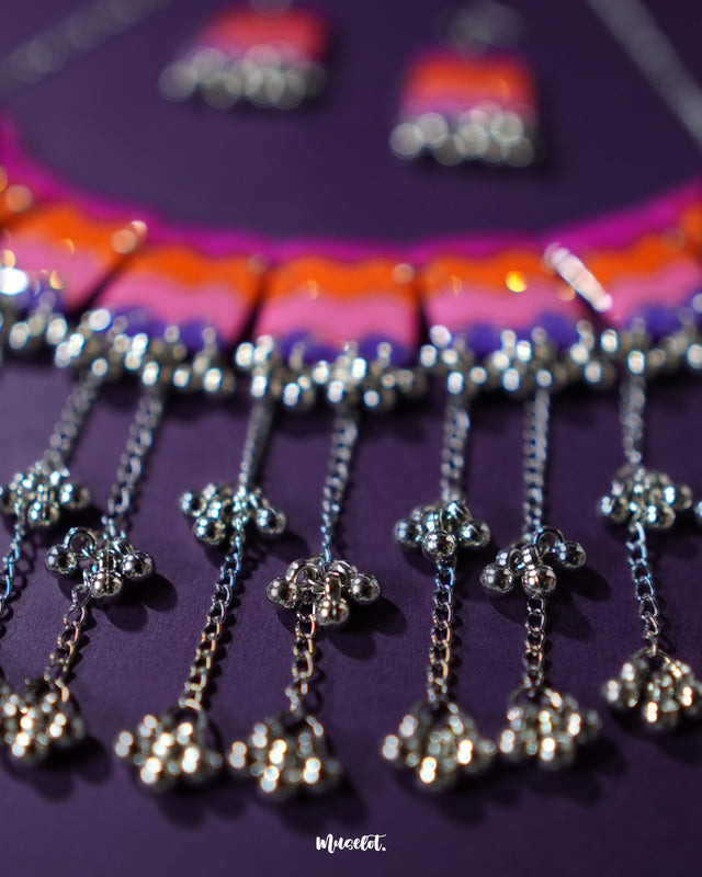 A close-up view of the Rangrezan handmade necklace set highlights the playful cluster of ghungroos, their metallic charm adding a rhythmic, festive touch to the colorful beads and intricate threadwork — Muselot.