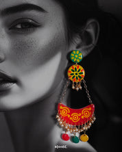 A close-up of a woman wearing the Rangsiya chandbali earrings, showcasing their vivid red, yellow, and green enamel work, pearl bead detailing, and colorful dangling discs — an eye-catching blend of tradition and playfulness that lights up the look — Muselot.