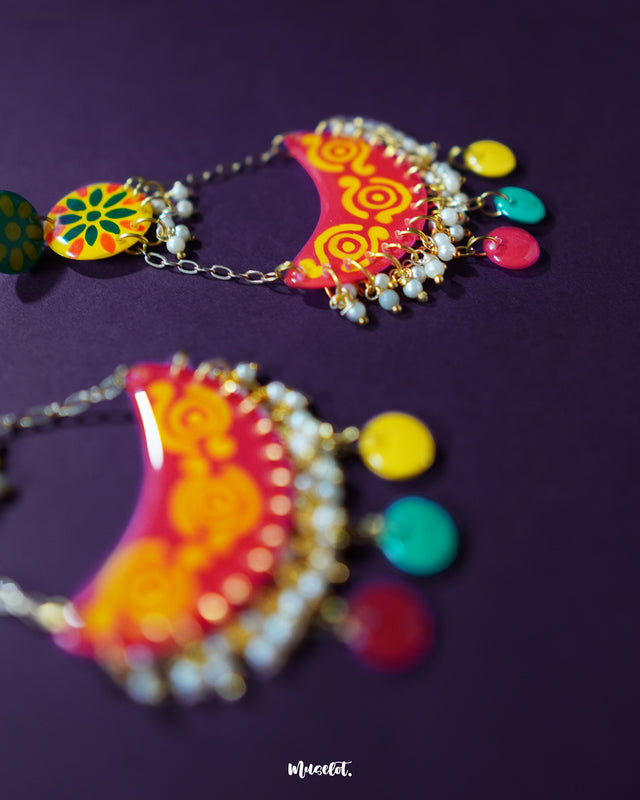 A close-up of the Rangsiya colorful chandbali earrings showcasing their vibrant red and yellow hand-painted detailing, delicate pearl drops, and playful multicolor danglers hanging from golden chains — Muselot.