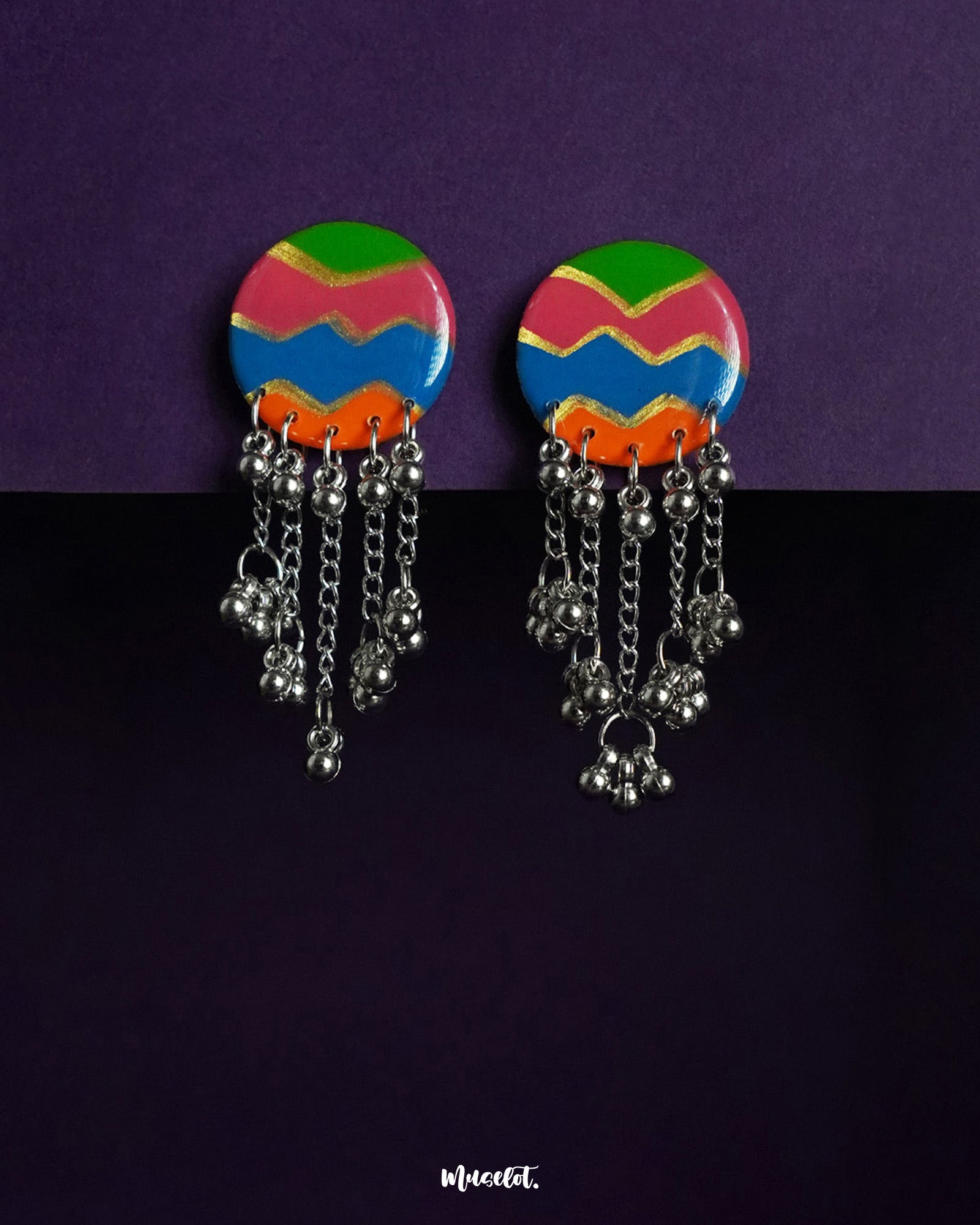A vibrant pair of round handcrafted earrings featuring bold zigzag patterns in green, pink, blue, and orange, finished with dangling silver chains and clustered beads—bursting with festive charm and playful movement – Muselot.