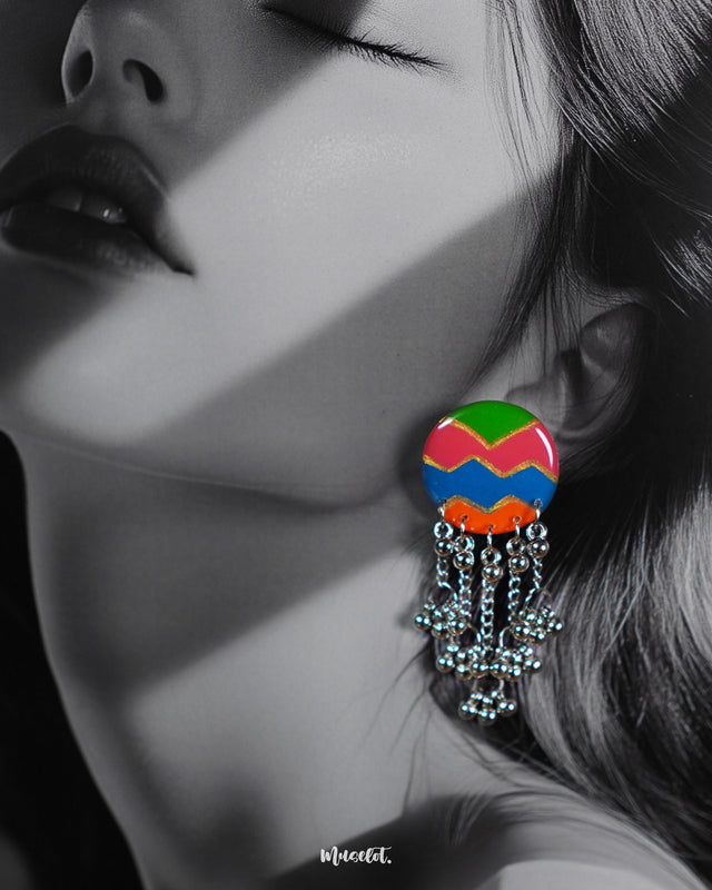 A close-up of a woman wearing the Rangtarang chain earrings, showcasing their vivid hand-painted round tops in green, pink, blue, and orange zigzags, with silver bead chains cascading down—capturing a joyful fusion of folk artistry and bold individuality – Muselot.