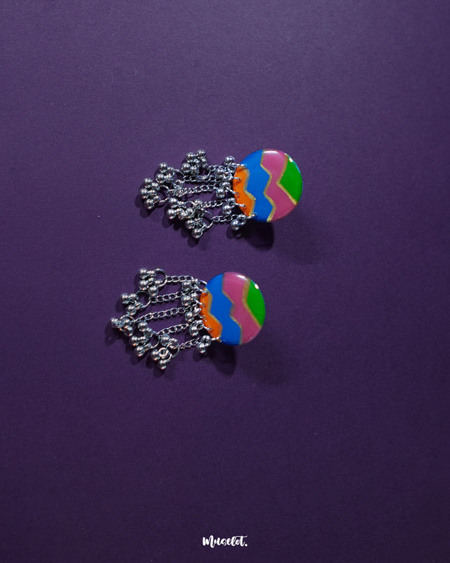 Rangtarang colorful long chain earrings showcasing a vibrant fusion of hand-painted zigzag patterns in green, pink, blue, and orange, paired with dangling silver chains and metallic beads that dance with every movement, capturing the essence of playful elegance – Muselot.