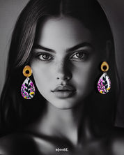 A model wearing the Raushanbahaar handmade floral drop earrings, featuring teardrop-shaped pieces adorned with vibrant floral artwork in pink, green, and yellow hues, anchored by golden abstract studs for a contemporary ethnic fusion — Muselot.