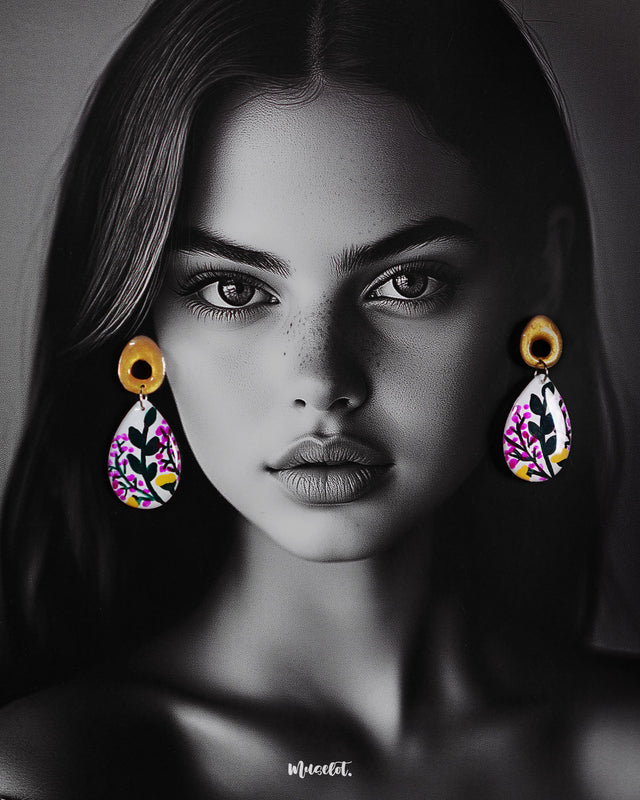 A model wearing the Raushanbahaar handmade floral drop earrings, featuring teardrop-shaped pieces adorned with vibrant floral artwork in pink, green, and yellow hues, anchored by golden abstract studs for a contemporary ethnic fusion — Muselot.